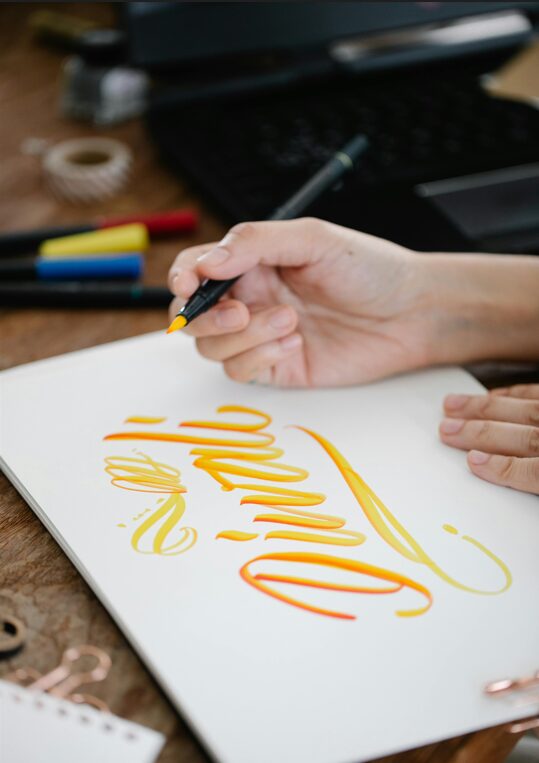 Person Practicing Elegant Handwriting with Pens and Paper